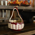 A decorative hand-crafted gourd basket with a merlot red body, natural gourd handle, and woven white reed, displayed on a dark wooden surface.