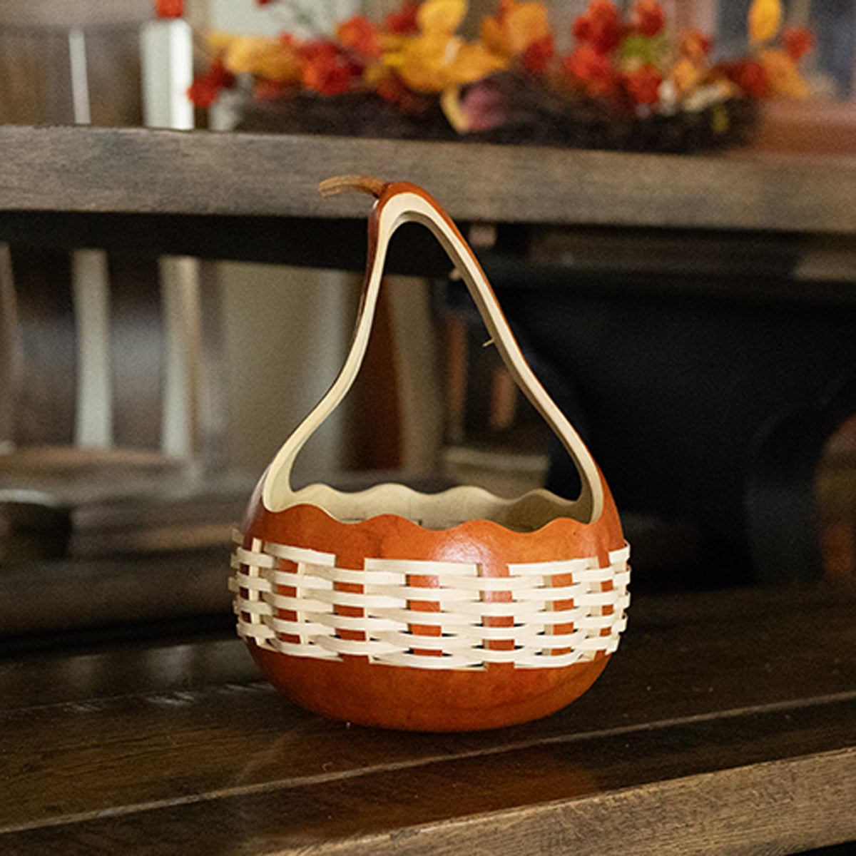 A small decorative basket made from a gourd with woven white reed on the lower half and a curved handle, placed on a dark wooden surface.