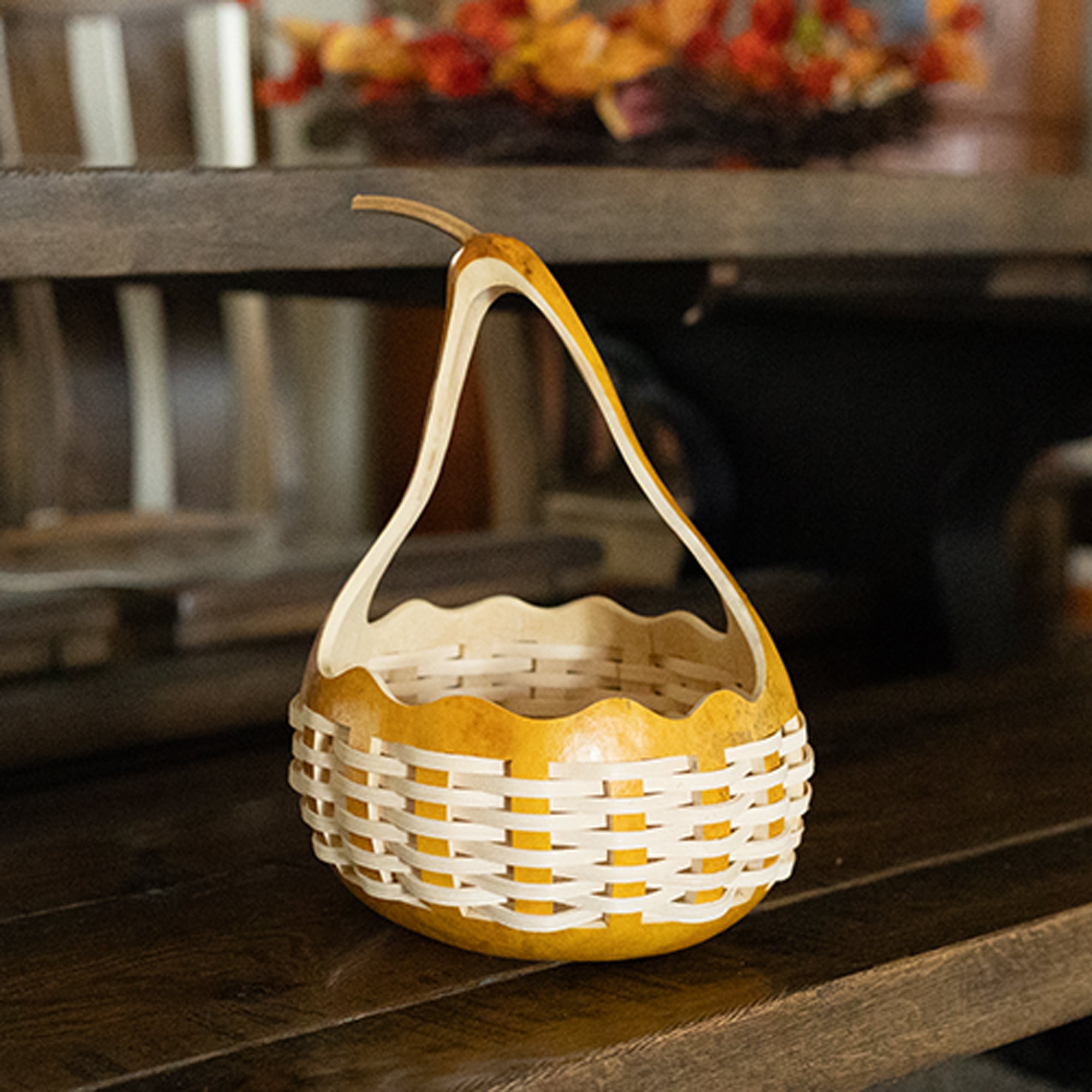 A small decorative basket made from a natural gourd with a woven white reed around the gourd, displayed on a dark wooden surface.