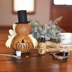 Two gourd turkeys with decorative details, one larger with a pumpkin design and one smaller with a leaf design. Both have black top hats and are displayed on a wooden surface.